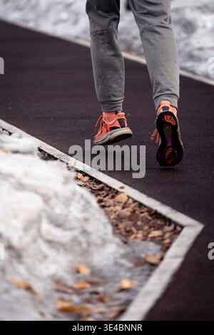 Ein Läufer in heller Sportausrüstung joggt auf einem freigelegten Weg, umgeben von Winterschnee Stockfoto