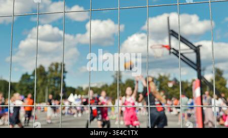 Blick auf ein Streetballspiel im Freien durch einen Maschendrahtzaun mit verschwommenem Hintergrund. Stockfoto