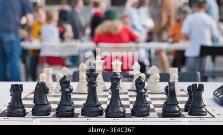 Schwarze Schachfiguren auf einem Brett zu Beginn eines Spiels mit verschwommenem Hintergrund für Turniere im Freien. Stockfoto
