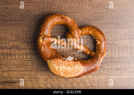 Eine frisch gebackene, gesalzene deutsche Brezel liegt auf einem rustikalen Holztisch mit goldbrauner Kruste, groben Salzkristallen und einer warmen, einladenden Textur Stockfoto