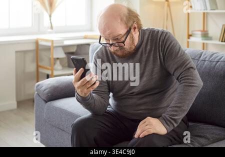 Innenaufnahme eines ernsthaften bärtigen älteren Mannes in Brille, fokussiert auf Smartphone-Bildschirm, um E-Mail-Box zu überprüfen Stockfoto