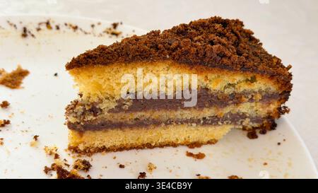 Nahaufnahme eines letzten Stücks mehrschichtiger Gluten- und laktosefreier Biskuitkuchen mit Schokoladencreme auf einer weißen Platte Stockfoto