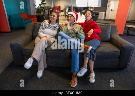 Verschiedene Kollegen, die in der Bürolounge auf einem Holzkohlesofa sitzen, tragen Urlaubspullover und Geweih Stockfoto