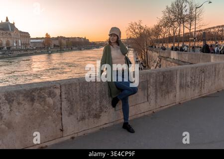 Frau, die auf einer Brücke in paris steht und den Wadenfluss bei Sonnenuntergang beobachtet, verkörpert Unabhängigkeit und die Freude an Alleinreisen in der european citi Stockfoto