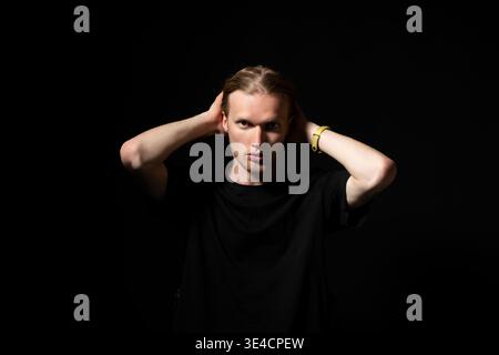 Junger hellhaariger Mann mit intensivem Blick, der den Kopf hält und Stress oder Angst spürt, ein dramatisches Studio-Porträt mit dezenter Beleuchtung und Kopierraum Stockfoto