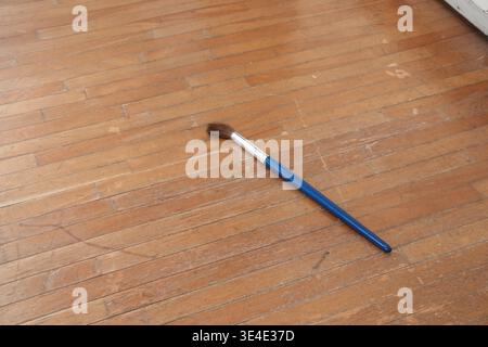 Die blaue Bürste liegt auf abgenutztem Holzboden. Der Griff glänzt mit glatter, polierter Oberfläche. Borsten wirken weich und leicht abgenutzt. Einfache, ruhige Szene e Stockfoto