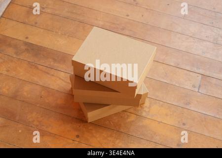 Drei einfache Kartons liegen auf warmen Holzdielen. Jede Box ist ordentlich gestapelt, die Kanten sind sauber und nicht markiert. Das sce wird durch natürliches Licht beleuchtet Stockfoto