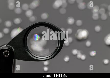 Nahaufnahme einer Lupe mit Blick auf funkelnde Edelsteine. Hintergrund zeigt verschwommene, glitzernde Steine. Perfekt für Schmuckdesign, Gemologie oder lu Stockfoto