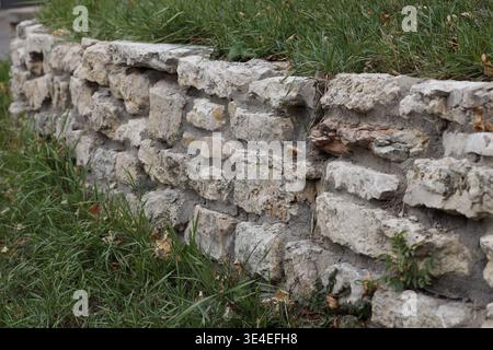 Gemauerter Kalksteinblock Landschaftsmauer mit grünem Gras, überwachsendes Laub (Panorama, Weitwinkel) Stockfoto