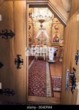 Blick durch eine offene Tür auf eine christlich-orthodoxe Kirche mit Taufsockel und vielen Ikonen von jesus und Heiligen. Kleines gemütliches hölzernes Chu Stockfoto