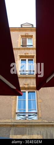 Metz, Fenster an einer Hausfassade, eingerahmt von Sonnenschirmen. Vertikale Aufnahme mit niedrigem Winkel Stockfoto