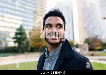 Junger Erwachsener lateinamerikanischer Geschäftsmann, der draußen mit Ohrstöpseln lächelt Stockfoto