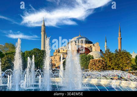 Der Brunnen fließt im Vordergrund, während die Hagia Sophia in Istanbul hoch steht. Die Leute laufen zu Fuß und genießen die Aussicht in der späten Nachmittagssonne. Stockfoto