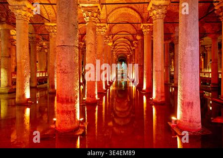 Besucher spazieren bei Nacht durch die Zisterne der Basilika in Istanbul, umgeben von beleuchteten Säulen und Wasser reflektierendem Licht. Stockfoto