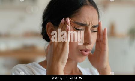 Krank krank erschöpft Arabische indische Frau zu Hause leiden Kopfschmerzen Migräne Schmerzen müde Frau mit Kopf gestresst ungesundes Gefühl unwohl Gesundheit Stockfoto