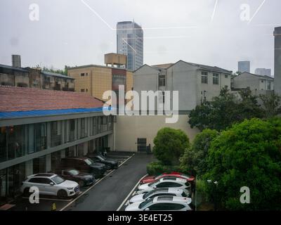 Wuhan, China - 11. April 2025: Erhöhter Blick auf einen Außenparkplatz mit geparkten Autos, umgeben von flachen und hohen Gebäuden. Das ima Stockfoto