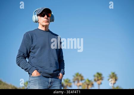 Mann mit Kopfhörern und Sonnenbrillen draußen, blauer Himmel Hintergrund Stockfoto