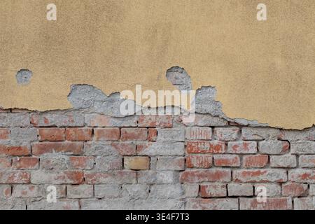 Alte Ziegelmauer mit abziehendem gelbem Gips Stockfoto