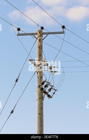 Versorgungsmast mit Freileitungen und Isolatoren gegen klaren blauen Himmel. Infrastrukturkonzept für Stromverteilung und Kommunikation Stockfoto