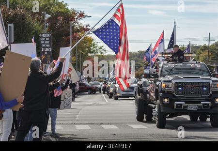 Eine Karawane von Pickup-Trucks mit Trump Vance-Branding und mit Stacheln versehenen Rädern steht den No Kings-Demonstranten gegenüber, die US-Flaggen schwenken und ein antifaschistisches Schild halten. Stockfoto