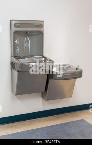 Moderner Trinkwasserbrunnen mit an der Wand montierter Flaschenfüllstation, saubere Trinkgeräte im öffentlichen Innenbereich mit Kopierraum Stockfoto