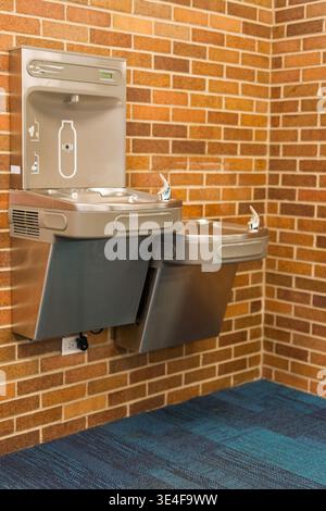 Moderner öffentlicher Trinkwasserbrunnen mit Flaschenfüllstation an Backsteinmauer im Innenbereich, saubere Trinkwasserstation im öffentlichen Gebäude Stockfoto