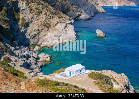 Die weiße Kapelle von Agia Anna mit ihrem Glockenturm befindet sich auf einem felsigen Vorsprung über einer türkisfarbenen Bucht auf Amorgos. Stockfoto