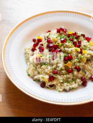Cremiges Risotto mit Granatapfelkernen und frischen Kräutern, serviert in einer weißen Schüssel Stockfoto