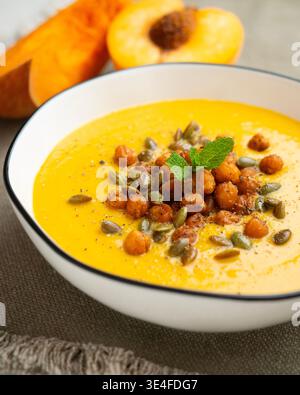 Cremige Kürbissuppe mit Pfirsich, garniert mit gerösteten Kichererbsen und Kürbiskernen Stockfoto