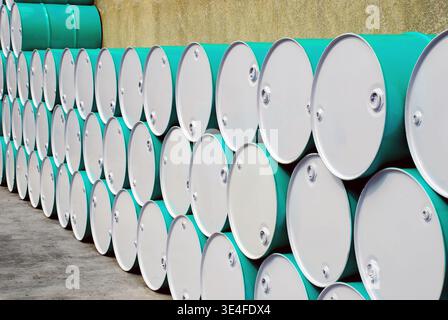 Reihen von gestapelten Türkis- und weißen Industriefässern. Nahperspektive von Metallchemikalienfässern, die an einer Betonwand in einem Außenbereich angeordnet sind Stockfoto
