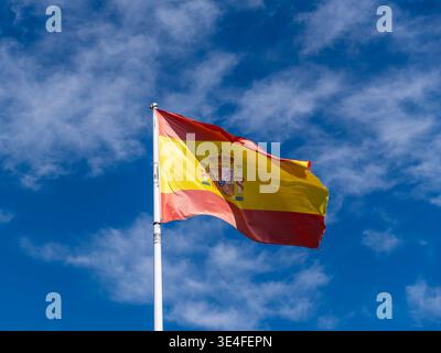 Spaniens Nationalflagge winkt vor einem blauen Himmel, leuchtendes Rot und Gelb mit dem königlichen Wappen, das Stolz und Erbe symbolisiert Stockfoto