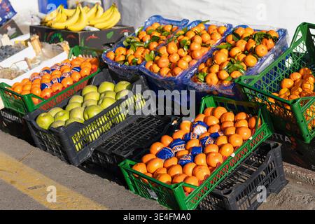 Sonniger Obstmarkt auf der Straße mit frischen Orangen, Mandarinen und grünen Äpfeln in bunten Plastikkisten. Lebhafte Basarszene im Freien in hellem Licht Stockfoto
