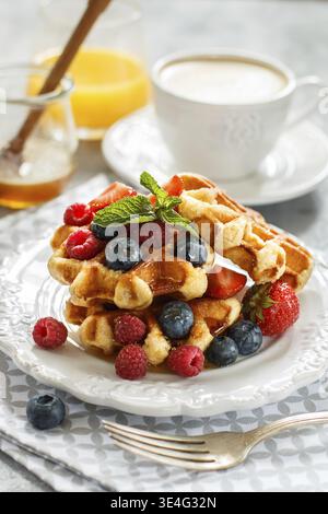 Essen, frische hausgemachte Waffeln mit Himbeeren, Erdbeeren, Heidelbeeren und Honig. Leckeres Frühstück mit Beeren, Cappuccino und Orangensaft. Se Stockfoto