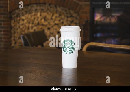 Starbucks Kaffeetasse aus Papier auf einem Holztisch in der Nähe eines Kamins, gemütliche Café-Atmosphäre. Portsmouth, Großbritannien, 3. Juli 2024 Stockfoto