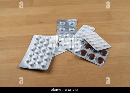 Pillen und Medikamente in Blisterpackungen, die auf einer hellen Holzoberfläche liegen und Gesundheit und Wohlbefinden darstellen Stockfoto