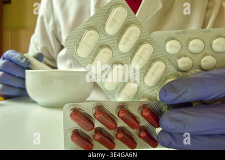 Apothekerhandschuhe bereiten Arzneimittel mit Mörtel und Stößel vor, wobei Blisterpackungen mit Pillen enthalten sind Stockfoto