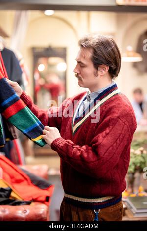 Geringerer Verbrauch und bewusstes Einkaufen, Hipster-Mann, der Strickwaren im Second-Hand-Shop aussucht. Stockfoto