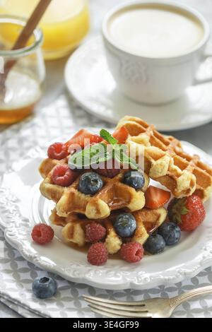 Essen, frische hausgemachte Waffeln mit Himbeeren, Erdbeeren, Heidelbeeren und Honig. Leckeres Frühstück mit Beeren, Cappuccino und Orangensaft. Se Stockfoto
