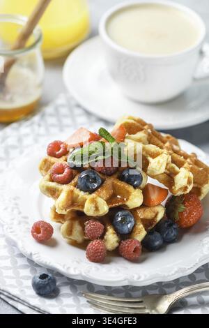 Essen, frische hausgemachte Waffeln mit Himbeeren, Erdbeeren, Heidelbeeren und Honig. Leckeres Frühstück mit Beeren, Cappuccino und Orangensaft. Se Stockfoto
