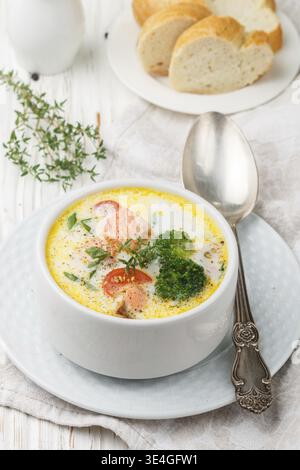 Essen, Lachscremesuppe mit Gemüse - Kartoffeln, Karotten, Tomaten und Brokkoli in einer weißen Schüssel auf hellem Holztisch Stockfoto