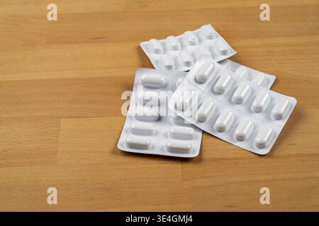 Weiße Kapselpillen in mehreren Blisterpackungen auf einer hellbraunen Holzoberfläche Stockfoto