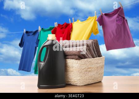 Wäschekorb mit sauberen Handtüchern und einer Flasche Waschmittel auf dem Tisch. Kleidung, die am Himmel trocknet Stockfoto
