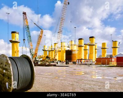 Stahlfundamente für Offshore-Windturbinen, die an einem Hafenkai gelagert und für den Transport und die Installation in einem Ostsee-Windpark vorbereitet werden. Stockfoto