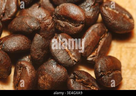 Nahaufnahme gerösteter Kaffeebohnen auf einer hellen Holzoberfläche. Warme, minimale Komposition, ideal für Konzepte in Bezug auf Kaffee, Energie und Frühstück Stockfoto