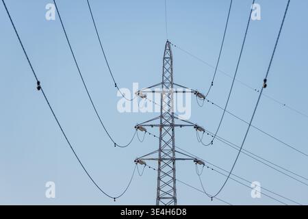 Hochspannungsgitter-Übertragungsturm, der mehrere Ebenen von Stromleitungen unterstützt, die sich in Oberleitungskurven über klaren blauen Himmel erstrecken. Stockfoto