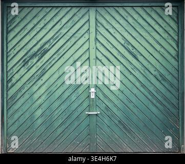 Symmetrische Nahansicht eines grünen Holztors mit diagonalem Dielenmuster und mittigem Griff, ideal für Textur, Geometrie und Fassadenmotive. Stockfoto