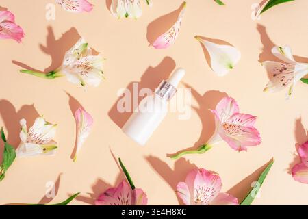 Kosmetische Serumflasche mit Alstroemerieblumen auf beigefarbenem Hintergrund. Minimale Schönheitskomposition. Draufsicht, flach, Modell. Stockfoto