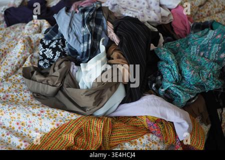 Kleidung stapelte sich auf einem Bett in einem unordentlichen Zimmer Stockfoto