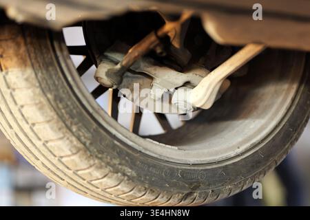 Eine Nahaufnahme einer Fahrzeugaufhängung und Bremsanlage zeigt das Rad, den Querlenker, die Spurstange und die Bremsscheibe von unten auf einer Hebebühne, 2026 Stockfoto
