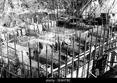 Nikolajewka, 1957. Slawjanskaja GRES. Ein großes Übersichtsfoto, das den massiven Bewehrungsrahmen aus Stahl feststellt, der sorgfältig für die Errichtung des Kraftwerks SlavGRES vorbereitet wurde. Zahlreiche Arbeiter werden beobachtet, wie sie sich über das komplizierte Stahlgitter in der großen Grube bewegen und aktiv daran arbeiten. Der Hintergrund zeigt umfangreiche provisorische Holzschalungs- und Gerüstsysteme. Dieses Vintage-Bild zeigt die beeindruckende Komplexität und den Umfang der Technik und zeigt fleißige friedliche Arbeit und Entwicklung im friedlichen Donbass vor dem Krieg. Stockfoto